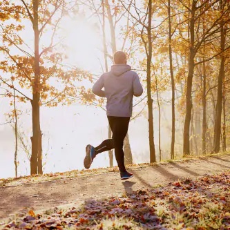 Herr mit Stoma joggt auf Waldweg im Herbst