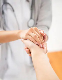 Eine medizinische Fachkraft hält beruhigend die Hand einer Patientin bzw. eines Patienten.