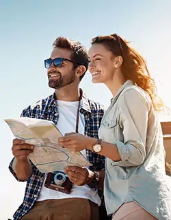 Ein Mann und eine Frau stehen im Freien, lächeln und schauen gemeinsam auf eine Landkarte.