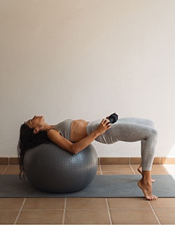 Frau führt eine Rücken- und Beckenbodenübung auf einem Gymnastikball aus.