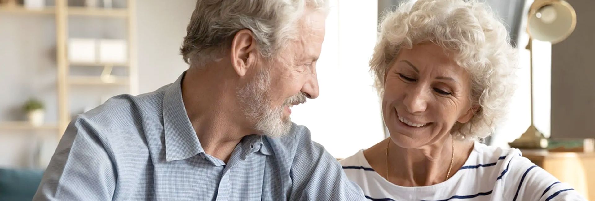 Ein älteres Paar sitzt am Tisch, schaut lächelnd auf ein Dokument und wirkt zufrieden.